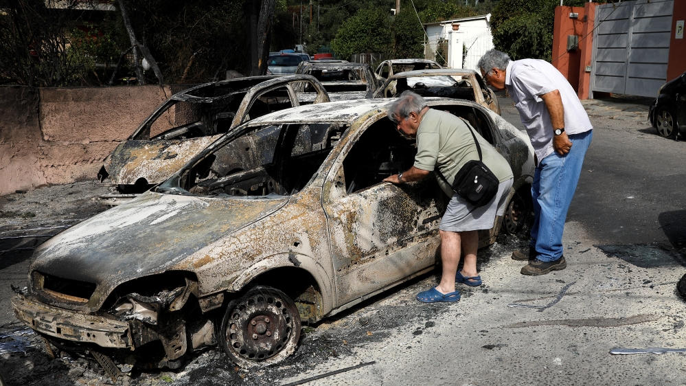 People look inside a burned-out car following a wildfire at the village of Mati [Alkis Konstantinidis/Reuters]