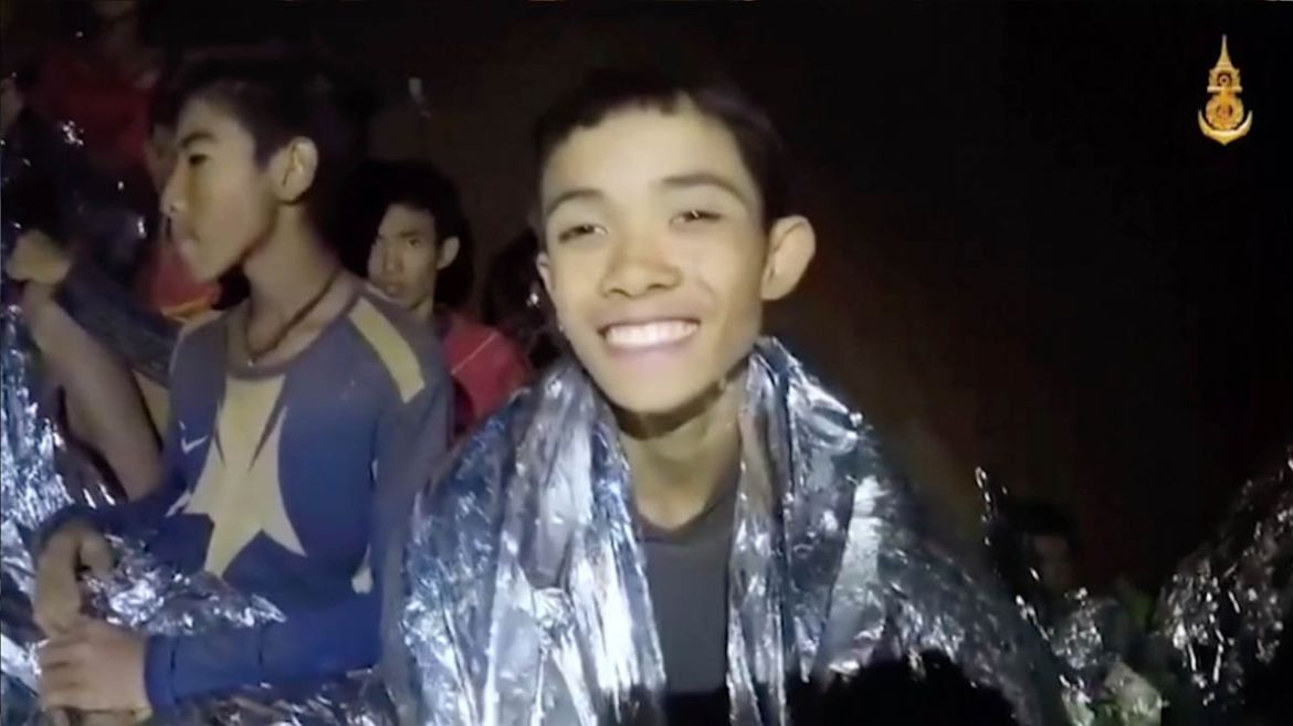 In this July 3, 2018, image taken from video provided by the Royal Thai Navy Facebook Page, a Thai boy smiles as Thai Navy SEAL medic help injured children inside a cave in Mae Sai, northern Thailand.