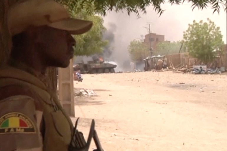 A still image taken from a video shows a Malian armed forces soldier standing guard as smoke and flames are pictured in the distance after a car bomb attack in Gao