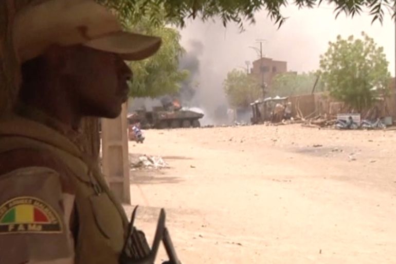 A still image taken from a video shows a Malian armed forces soldier standing guard as smoke and flames are pictured in the distance after a car bomb attack in Gao