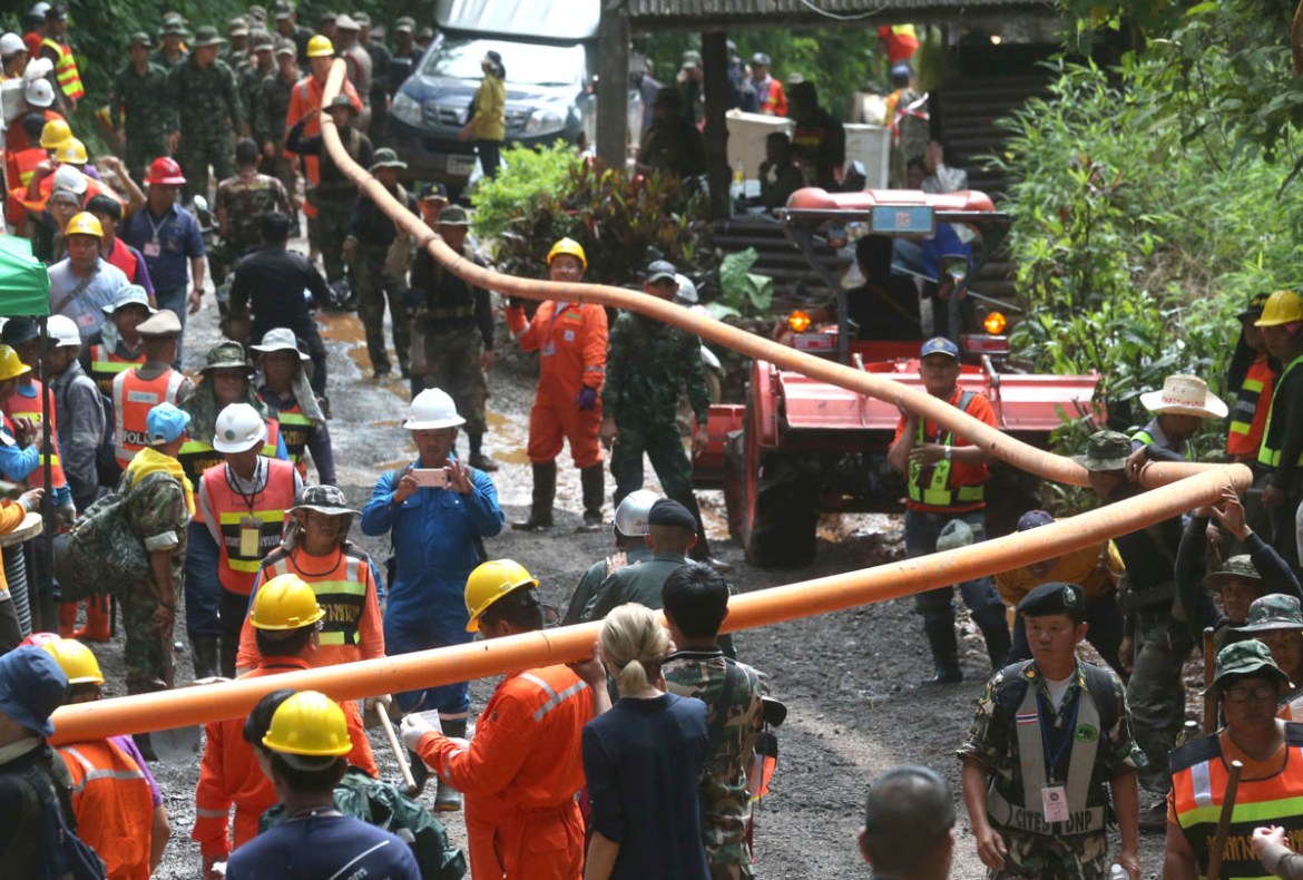 Rescuer carry water pipe makes their way up at the entrance to a cave complex where 12 boys and their soccer coach were trapped inside when heavy rains flooded the cave, in Mae Sai, Chiang Rai provinc