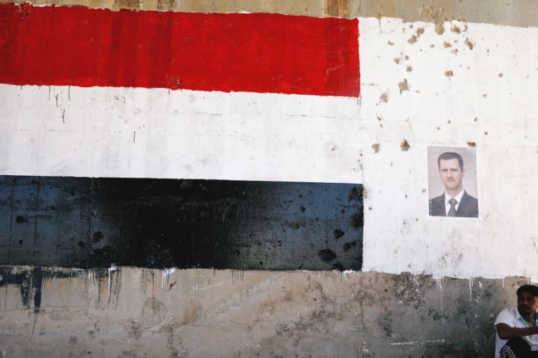 A man sits near a poster of Syrian President Bashar al Assad during the re-opening of the road between Homs and Hama in Talbisi, Syria