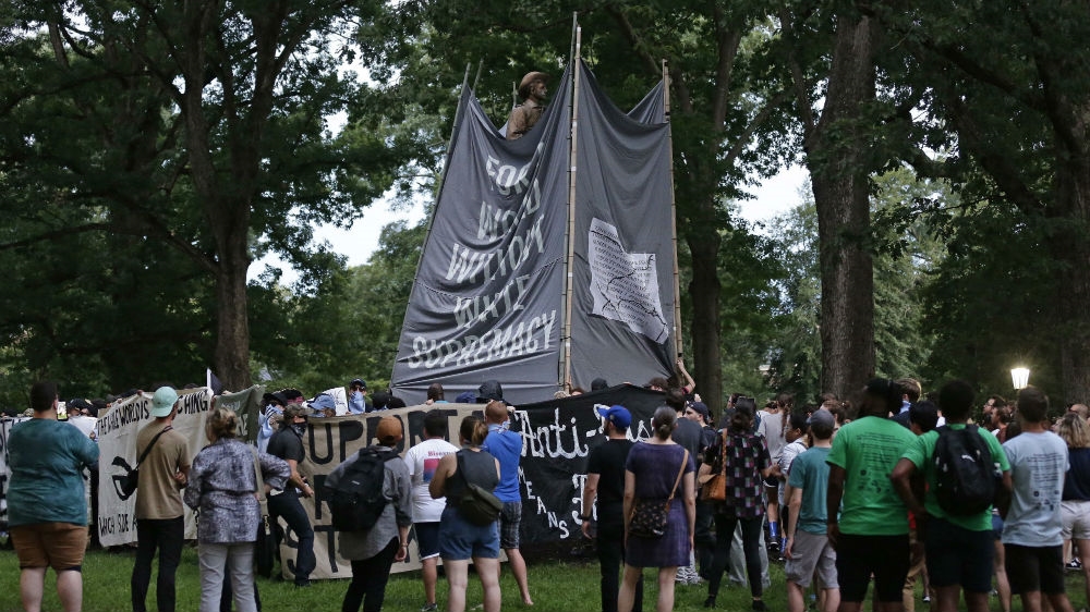 Banners are used to cover the Confederate statue known as Silent Sam as people gather during a rally to remove it [Gerry Broome/AP Photo] 