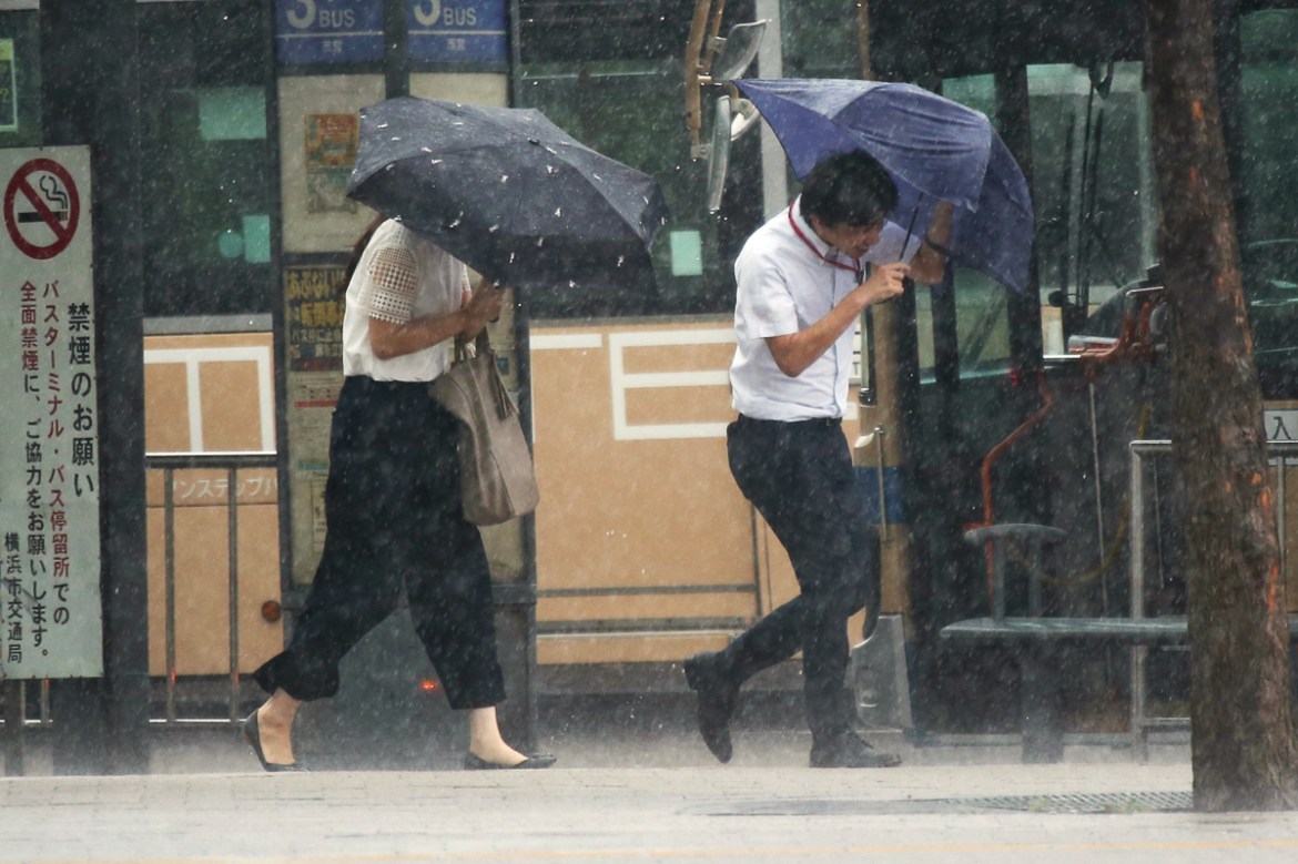 Pedestrians try to hold their umbrellas while struggling with strong winds in Yokohama, near Tokyo, Tuesday, Sept. 4, 2018. Heavy rain and crashing surf were striking western Japan as powerful Typhoon