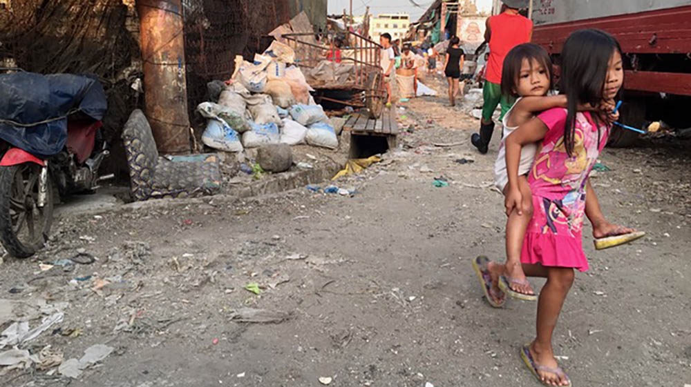 A young girl carrying a toddler walks towards a community room where Bahay Tuluyan delivers hot meals for children each week [Anne Bouleanu/Al Jazeera]