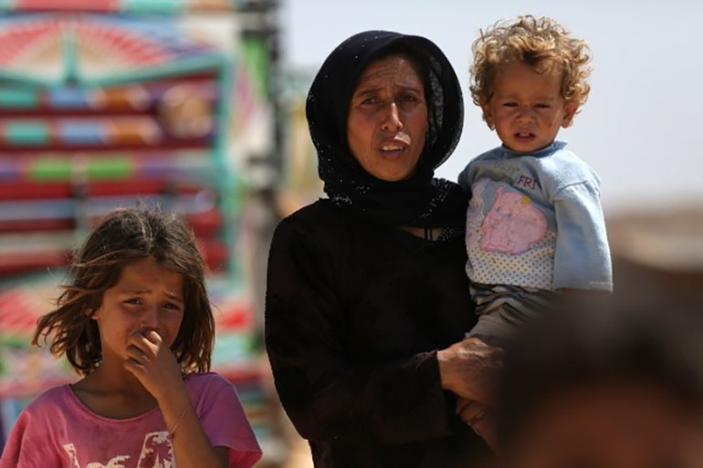 A woman who fled her village in Syria''s Idlib province carries a child at a camp in Kafr Lusin near the border with Turkey in the northern part of the province on September 9, 2018. Regime and Russian