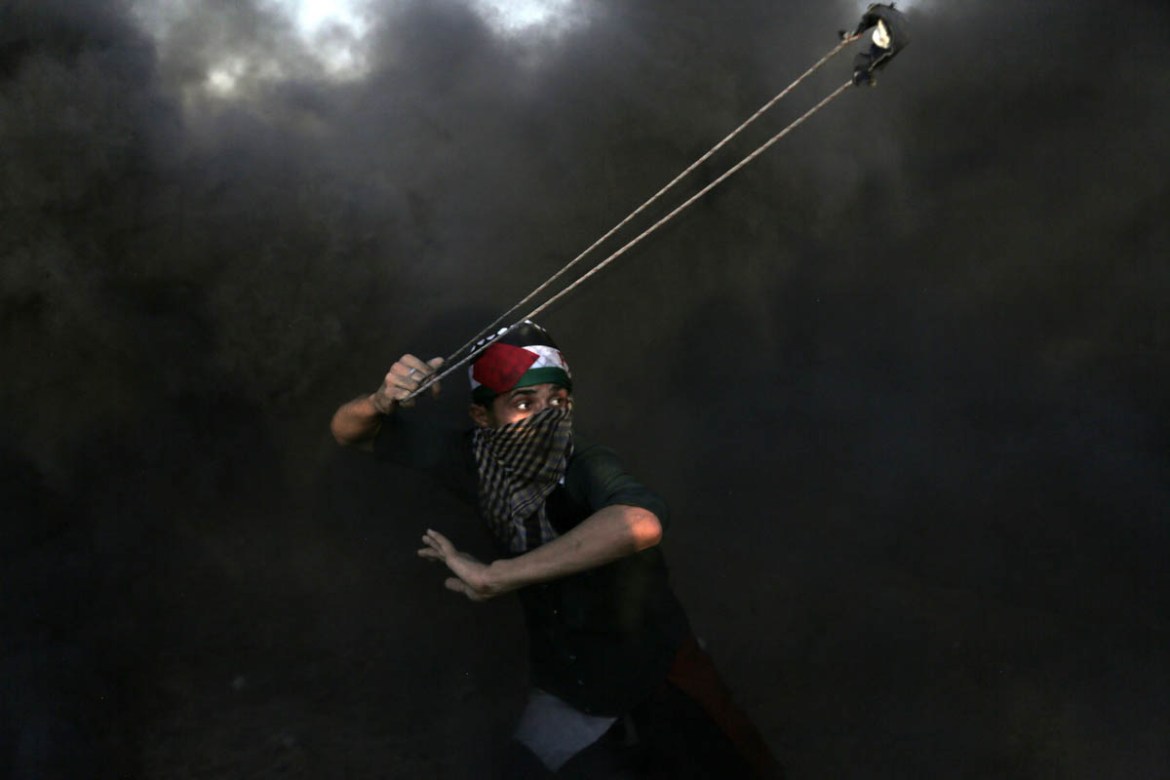 A Palestinian, engulfed in heay smoke, throws stones during the 26th Friday protest of Great March of Return, Gaza Strip, September 21, 2018. During the protests, Palestinians used burning tyres to h