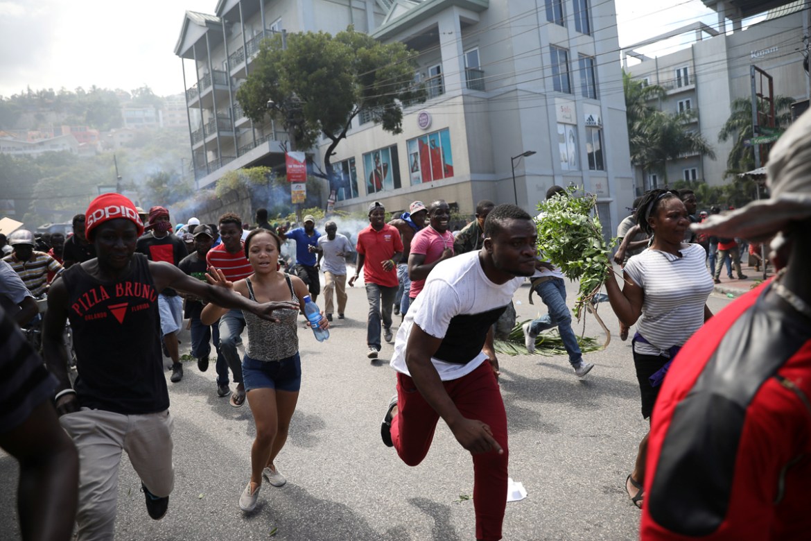 Protesters run away as Haitian National Police officers disperse them with tear gas during a march to demand an investigation into what they say is the alleged misuse of Venezuela-sponsored PetroCarib