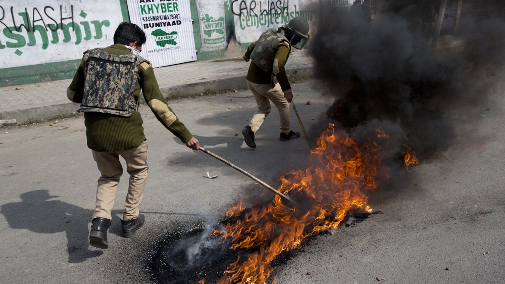 Indian policemen remove burning tires set up as road blockade by Kashmiri protesters near the site of a gunbattle in Srinagar [Dar Yasin/AP Photo]