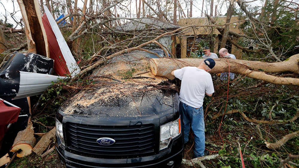 People cut away a tree that'll on a vehicle in the aftermath of Hurricane Michael in Panama City[Gerald Herbert/AP Photo]