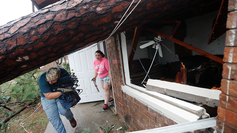 Megan Williams, left, and roommate Kaylee O'Brian take belongings from their destroyed home after several trees fell on the house during Hurricane Michael in Panama City [Gerald Herbert/AP Photo] 