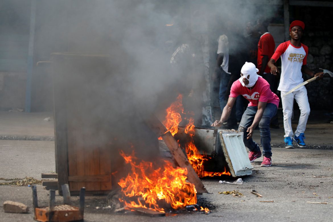 A protester pushes an old refrigerator into a burning barricade during a march to demand an investigation into what they say is the alleged misuse of Venezuela-sponsored PetroCaribe funds, in Port-au-