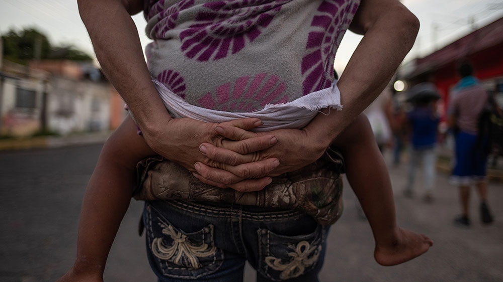 A Honduran man carries his two-year-old child while walking with a caravan en route to the United States [Adrees Latif/Reuters]