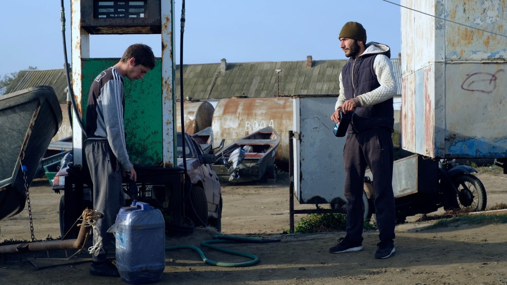 Fishermen fill canisters with petrol at the village port [Nikolay Korzhov/Al Jazeera]