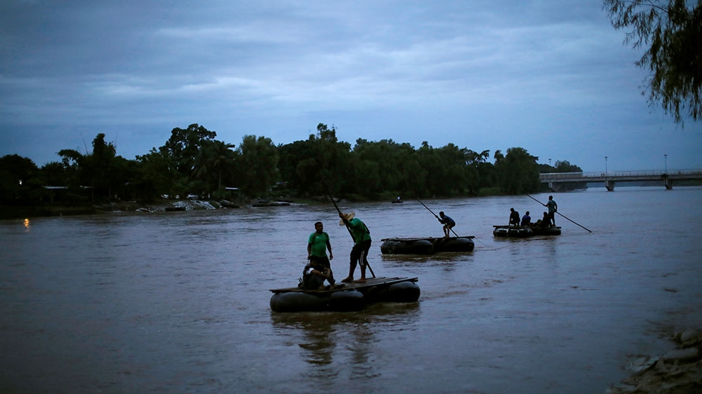 People manoeuvre rafts crossing the Suchiate river, a natural border between Mexico and Guatemala, as Honduran migrants, part of a caravan trying to reach the US, wait to cross into Mexico, in Tecun Uman, Guatemala [Ueslei Marcelino/Reuters]