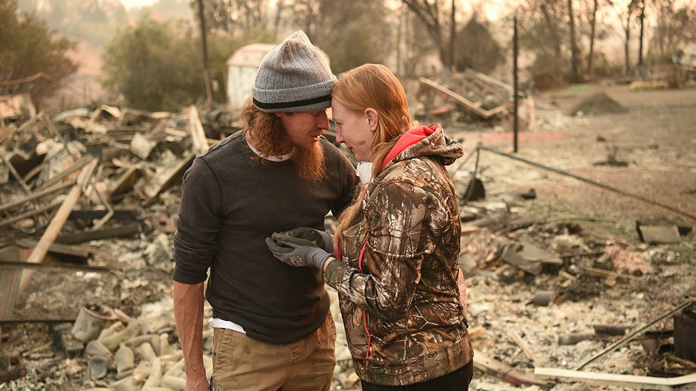 Ryan Spainhower and his wife, Kimberly, weep after finding a coin they had made during their honeymoon amidst the ashes of their home in Paradise [Josh Edelson/AFP]