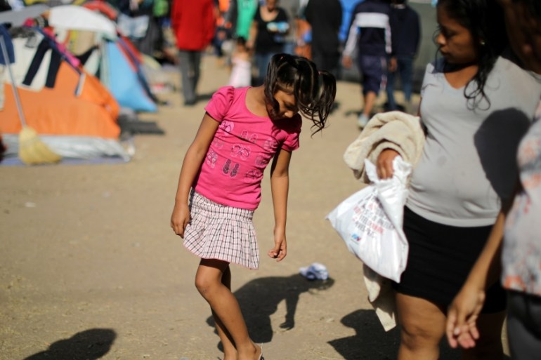 A girl tries on shoes as she waits with members of a caravan from Central America in Tijuana