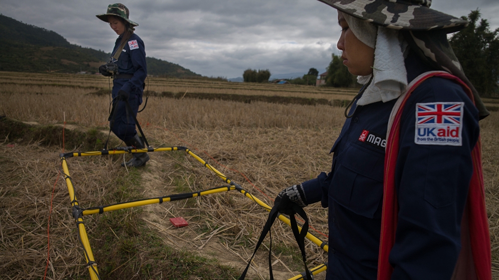 MAG personnel searching a rice paddy. Red painted wooden squares are used to mark metal detector signals, which are then inspected closely by other team members [Courtesy: MAG]
