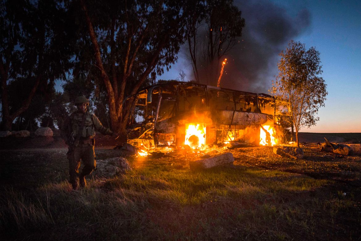 An Israeli soldier stands near a burning bus after it was hit by a mortar shell fired from Gaza near the Israel Gaza border, Monday, Nov. 12, 2018. Israel''s military says it is prepared to step up its