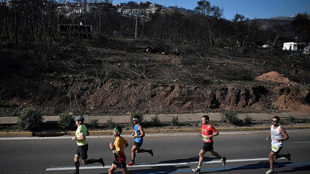 Marathon participants run past a burned-out area near Mati [Louisa Gouliamaki/AFP/Getty Images]