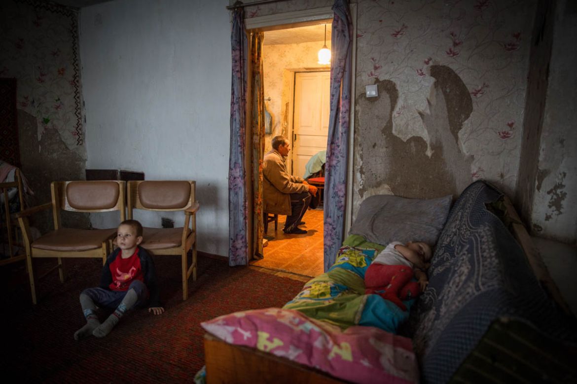 Iliya, 5, is watching TV while his father Viktor has a short rest in the kitchen. The youngest girl Aryna, 2, is having her afternoon nap. Their house was heavily damaged during the early days of war,