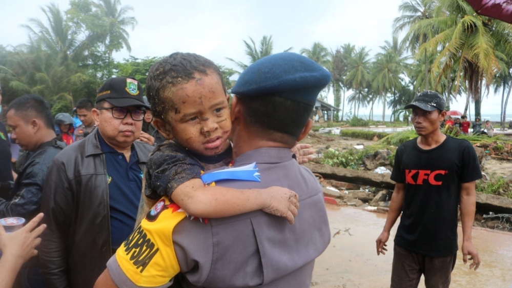 An injured boy is carried by a police officer from a hotel that collapsed due to the tsunami at Carita in Pandeglang, Banten province [Courtesy of Banten police headquarters/Handout via Reuters]