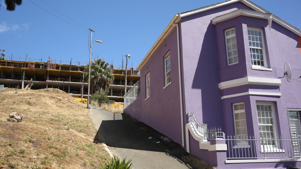 A new development in Bo Kaap rises above one of the neighbourhood's colourful traditional homes [Erica Jenkin/Al Jazeera] 