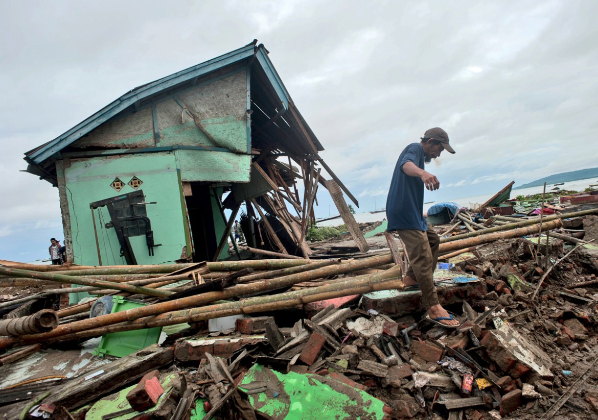 A man makes his way past a house badly damaged by a tsunami in Sumur, Indonesia, Monday, Dec. 24, 2018. Doctors worked to save injured victims while hundreds of military and volunteers scoured debris-