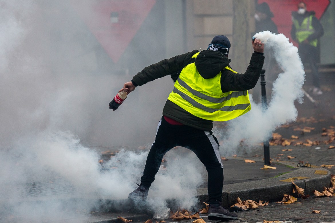 A demonstrator throws back a tear gas canister shot by police forces to disperse demonstrators during a protest on the adjacent streets to the Champs ElysE`es called for by the i`Gilets Jaunesi^ movem