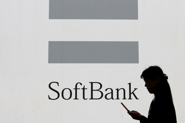 FILE PHOTO - A woman using a mobile phone walks past the logo of SoftBank Corp in Tokyo
