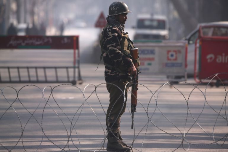 An Indian policeman stands guard behind concertina wire laid across a road leading to the Indian army headquarters in Srinagar
