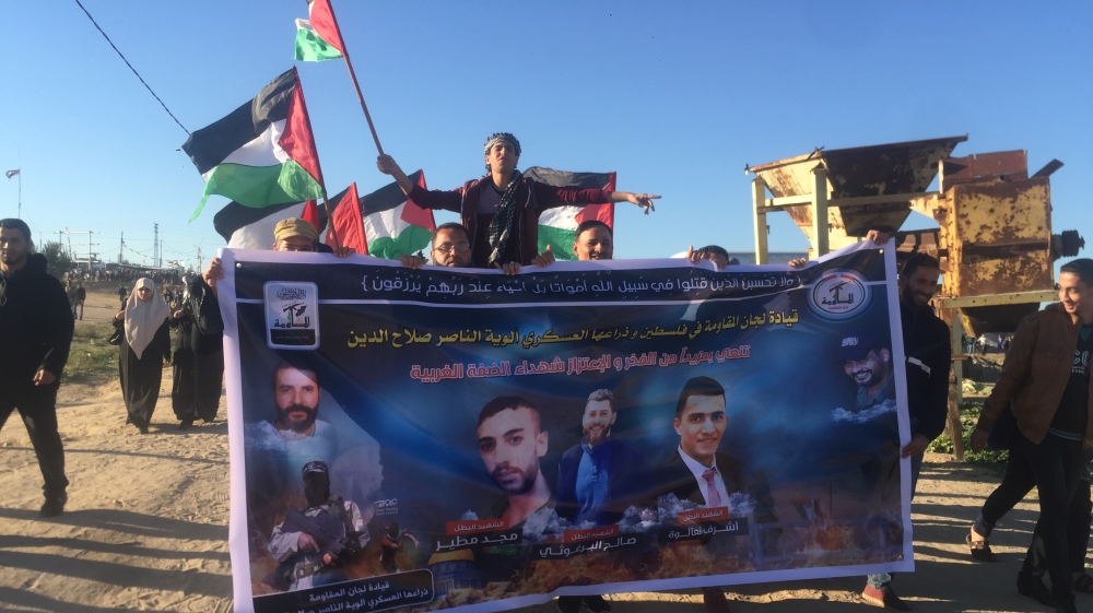 A protester in the Gaza Strip holds a poster with the pictures of the three Palestinians killed by Israeli forces overnight on Wednesday in the occupied West Bank [Maram Humaid/Al Jazeera]