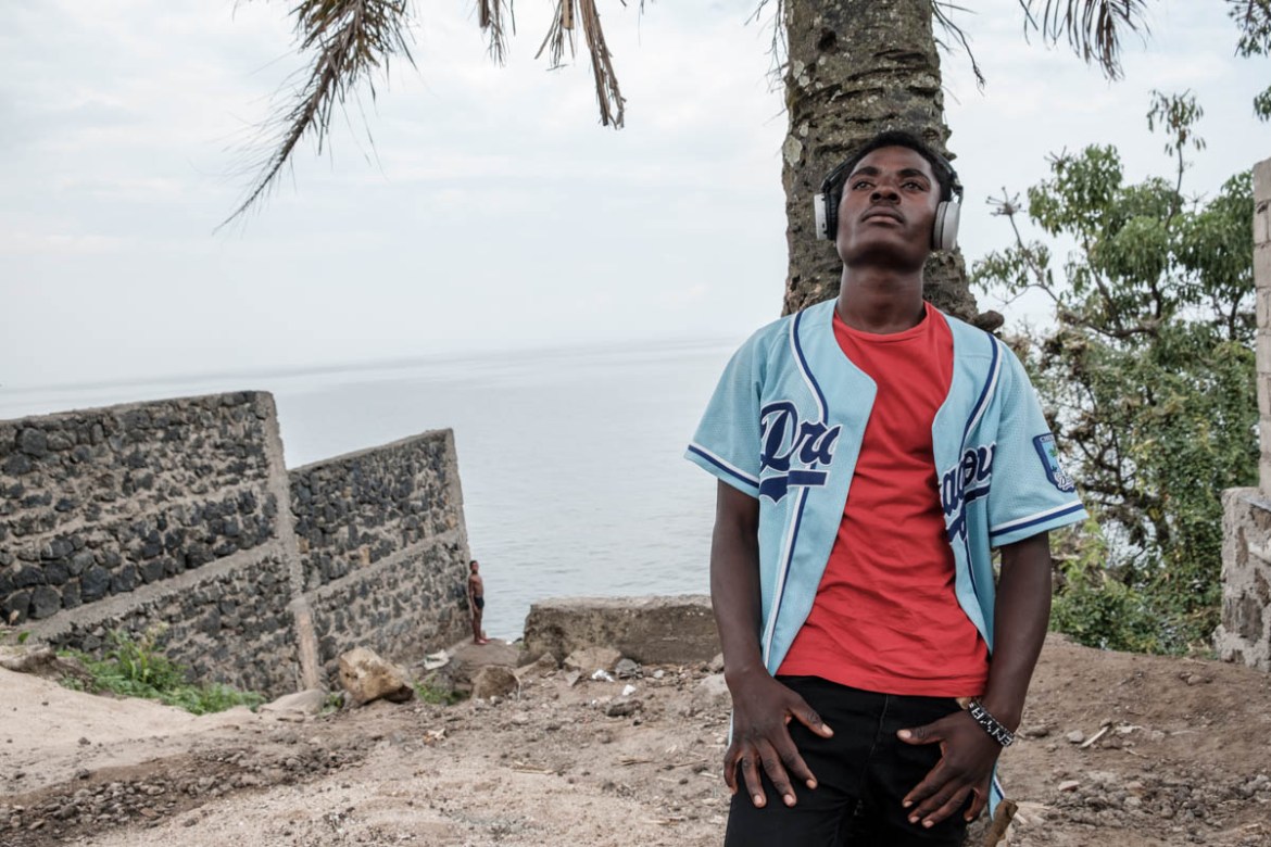 Enoke-B (24) lives right on the shores of Lake Kivu, surrounded by large misty mountains on the border with Rwanda. Big NGOs and UN agencies have their offices right in front of his “doorstep”.  
