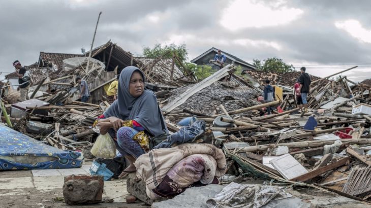 A tsunami survivor sits on a pice of debris as she salvages items from the location of her house in Sumur, Indonesia, Monday, Dec. 24, 2018. Doctors worked to save injured victims while hundreds of mi