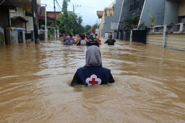 A volunteer wades through floods at a residential area in Makassar