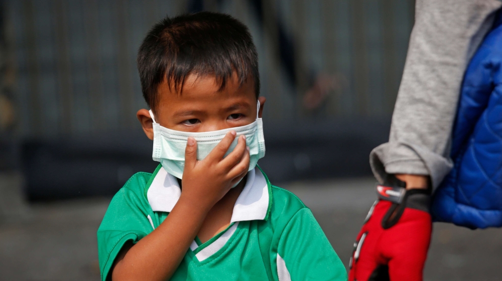 A young boy wears a protective mask as he's picked up from school [Sakchai Lalit/AP]