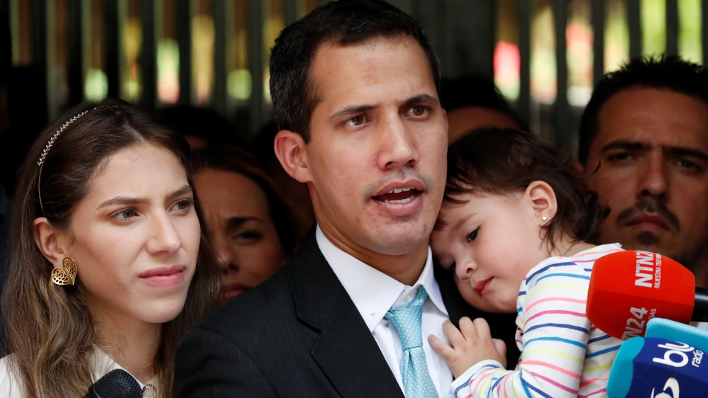 Guaido talks to media next to his wife Fabiana Rosales, while carrying their daughter outside their house [Carlos Garcia/Reuters]