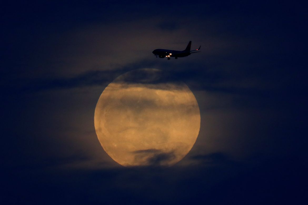 A full moon rises between clouds as a landing commercial jet approaches the airport before the start of a total lunar eclipse that is being called a ''Super Blood Wolf Moon'' in San Diego, California, U