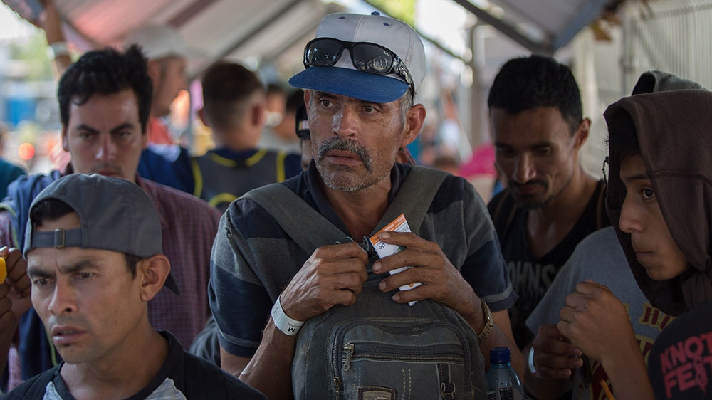 A group of men listen to instructions from a Mexican immigration official as they begin the process of obtaining their humanitarian visas [Jeff Abbott/Al Jazeera]