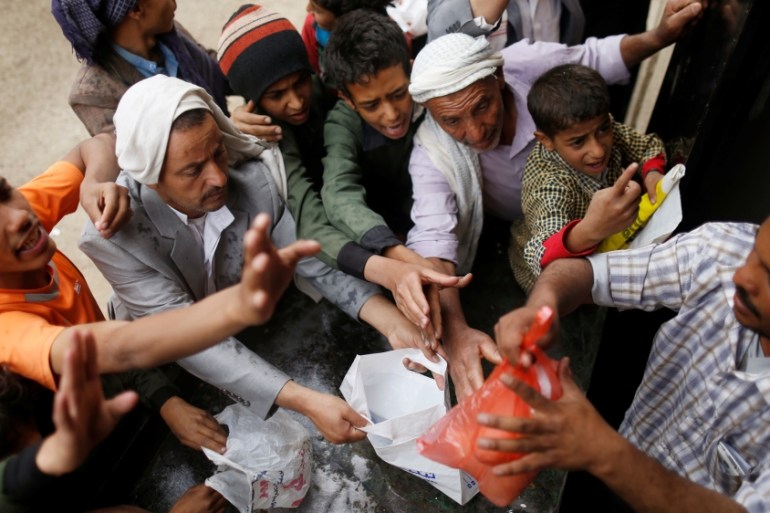 People gather to collect food rations at a food distribution center in Sanaa, Yemen