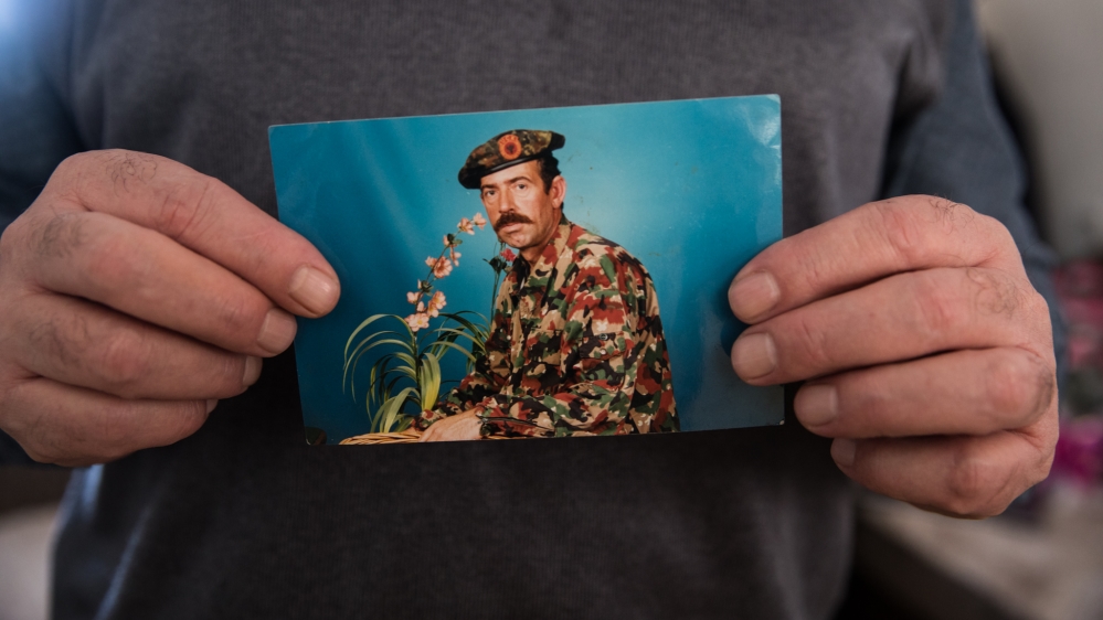Muhamet Bilalli holds a photo of himself when he was a KLA soldier. His brother was killed during the massacre at Racak [Valerie Plesch/Al Jazeera]