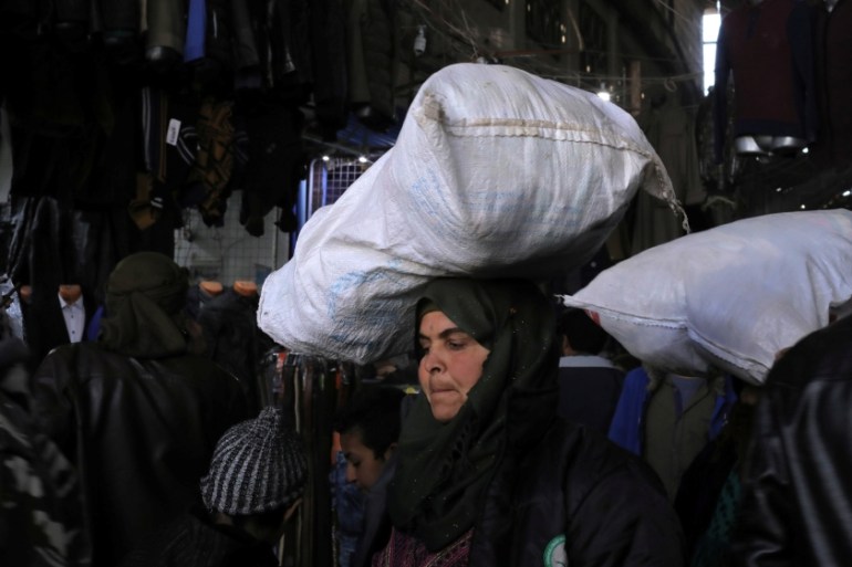 A woman holds a bag on her head at a souk in Manbij city