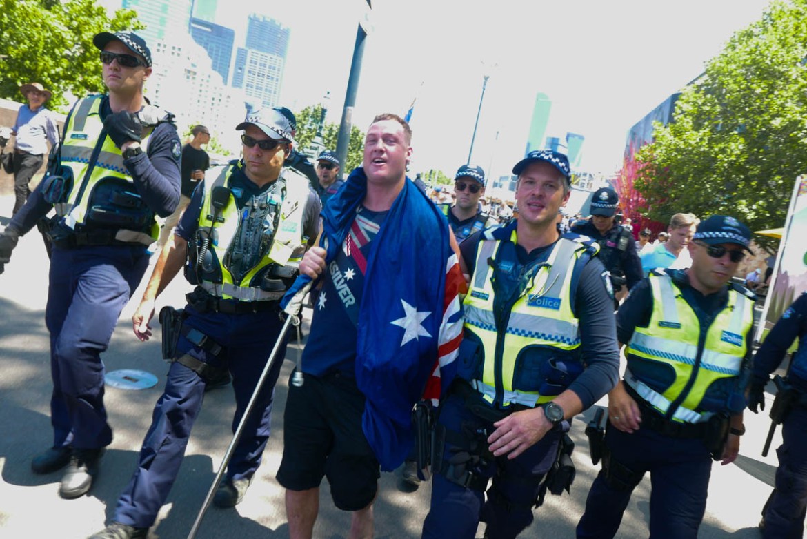 A far-right agitator is escorted away after an altercation, holding the Australian flag, which in recent times has become a symbol of white nationalism.