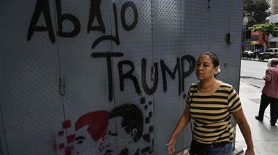 A woman walks past a graffiti depicting late Venezuelan president Hugo Chavez (R), President Nicolas Maduro and a legend reading 'down with Trump' in Caracas [Yuri Cortez/AFP] 