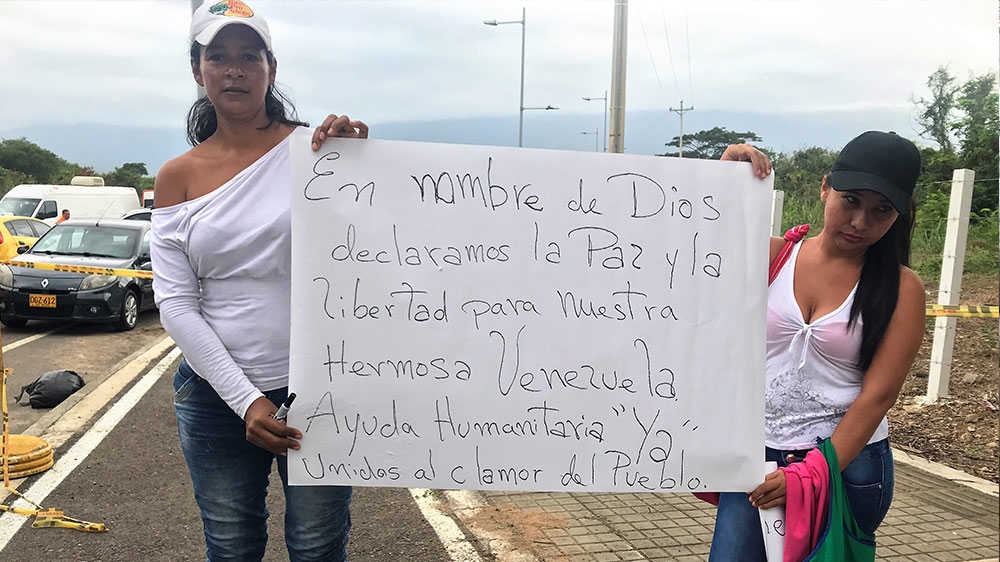 Omaria Perez, 44, was at the entrance of the Tienditas bridge on Friday morning, on her knees writing messages on placards. Her sign reads, 'In the name of God, we declare peace and freedom for our beautiful Venezuela. Humanitarian aid now. United public outcry' [Steven Grattan/Al Jazeera]