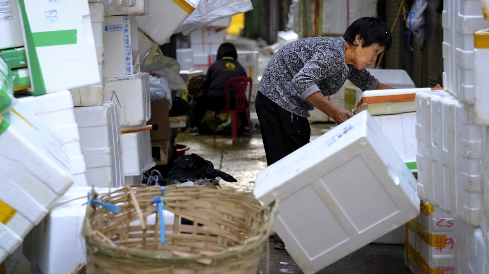 An elderly woman lifts trash in a Hong Kong market [Yupina Ng/Al Jazeera]