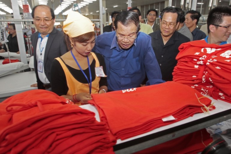 Prime Minister Hun Sen, center, leans over a garment worker during a visit to a factory outside of Phnom Penh, Cambodia,