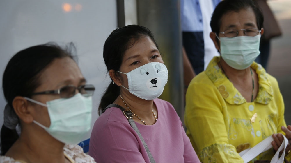 Women covering their face with protective masks at a bus stop in heavily polluted Bangkok last month [File: Sakchai Lalit/AP]