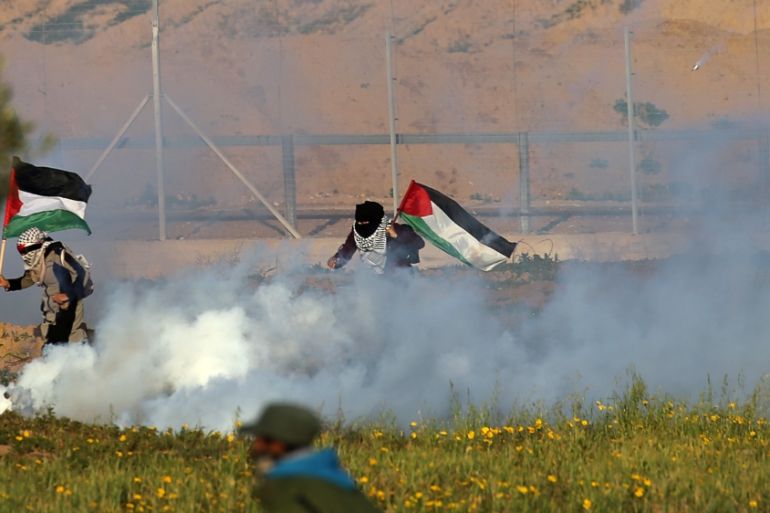 Women holding Palestinian flags run away from tear gas fired by Israeli forces during a protest at the Israel-Gaza border fence, in the southern Gaza Strip