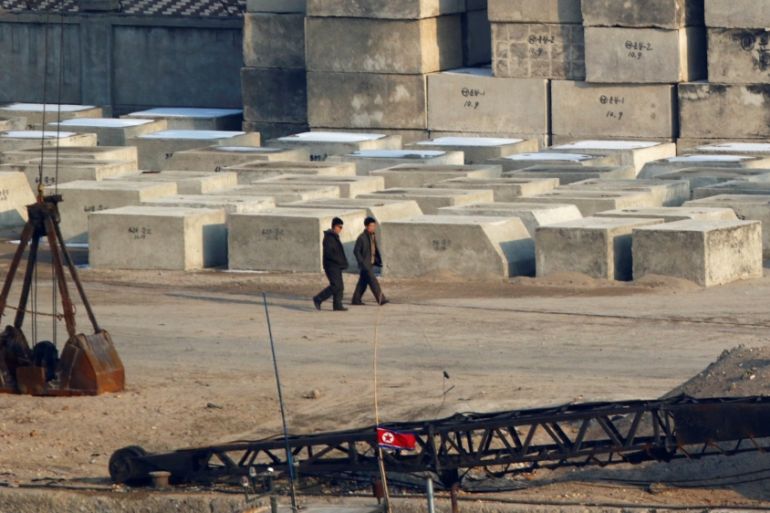 Men walk past concrete piers near a North Korean flag at a shipyard in Sinuiju